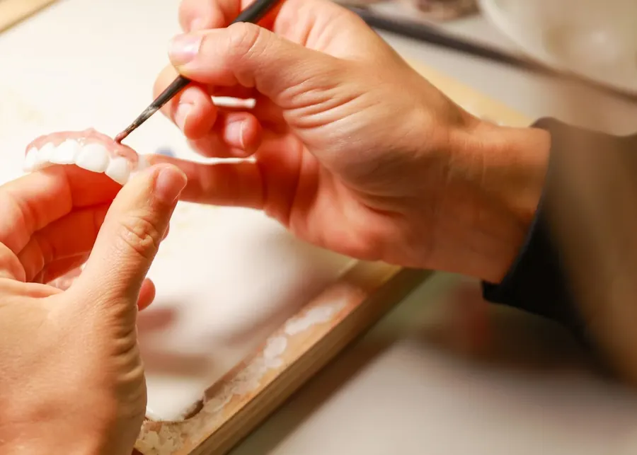 A lab technician's hands painting color onto a new set of denture teeth.