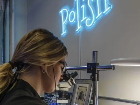A lab technician finishing a restoration at a microscope under a neon Polish sign.